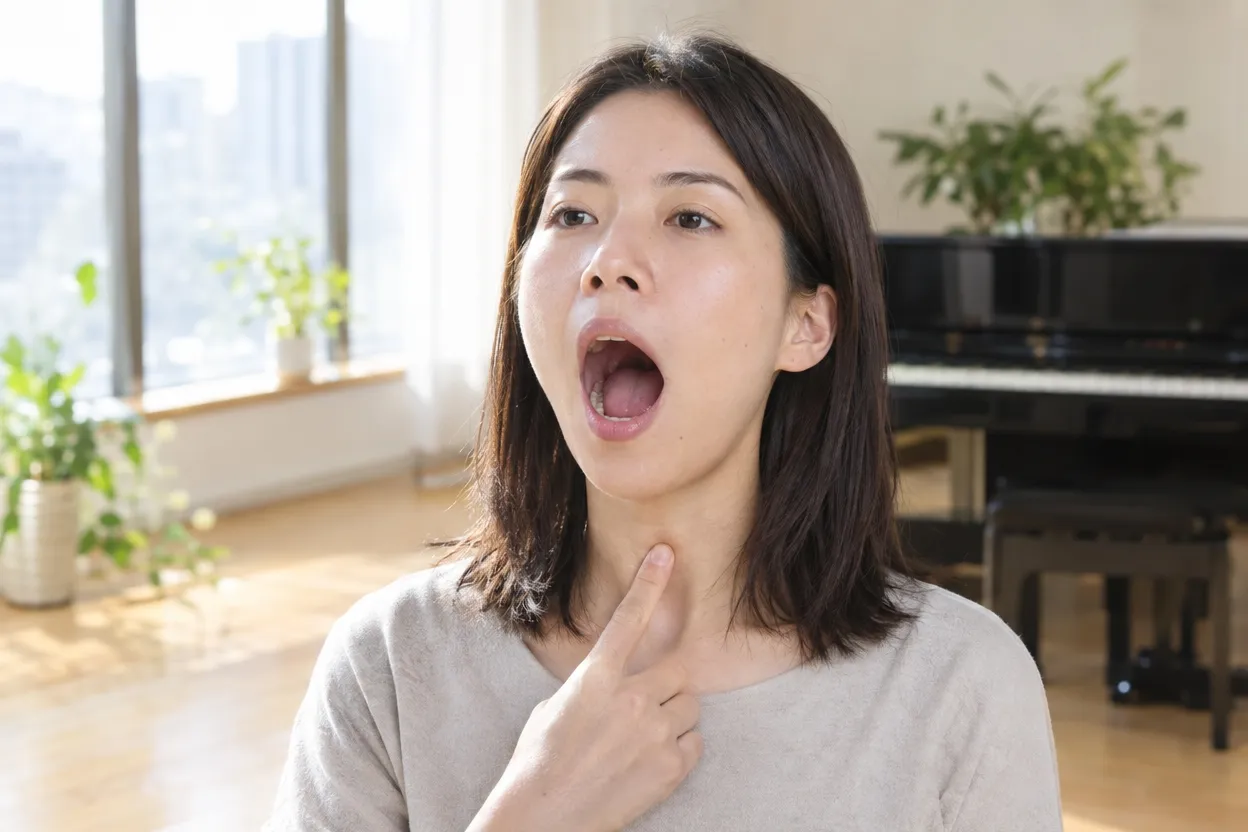 あくびの形で喉をゆるめ、のどに指を当てて確かめながら声を出す女性